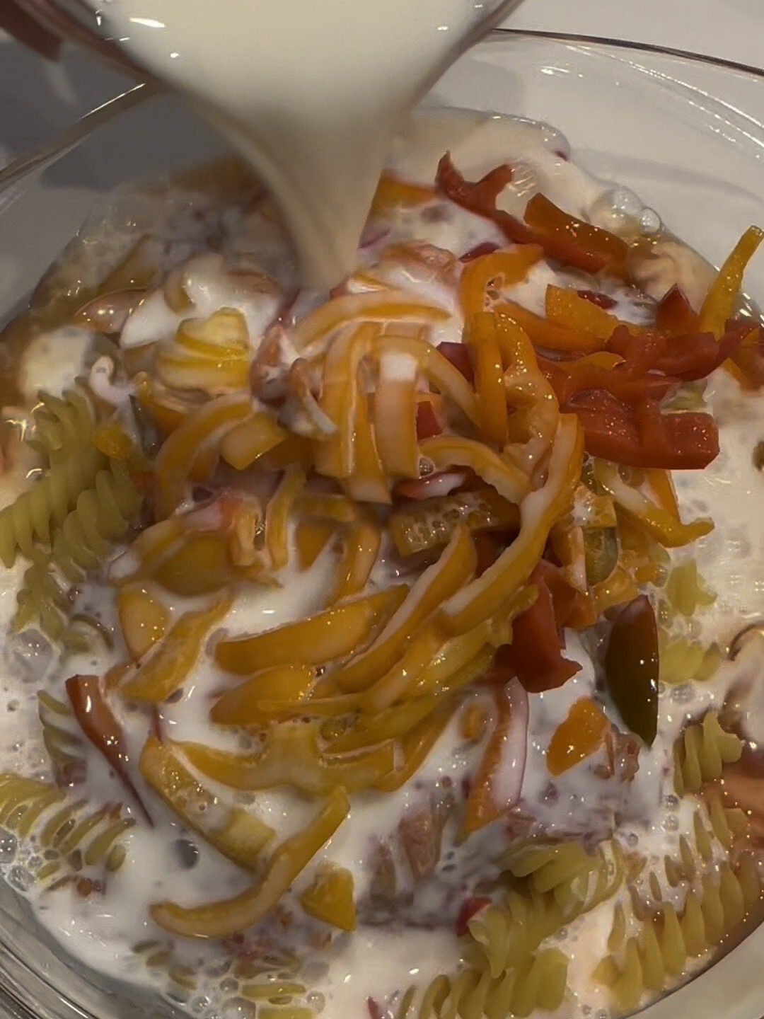 Zubereitung des cremigen Tomaten-Paprika-Auflaufs: Ungekochte Nudeln in einer Glasform werden mit Milch und getrocknetem Lauch für das Backen vorbereitet